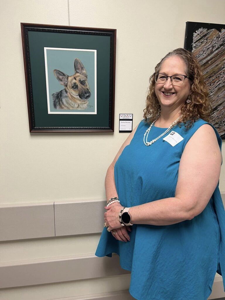 Tammy at her first exhibit, standing proudly in front of the colored pencil portrait of Gwendolyn, a beloved German Shepherd.